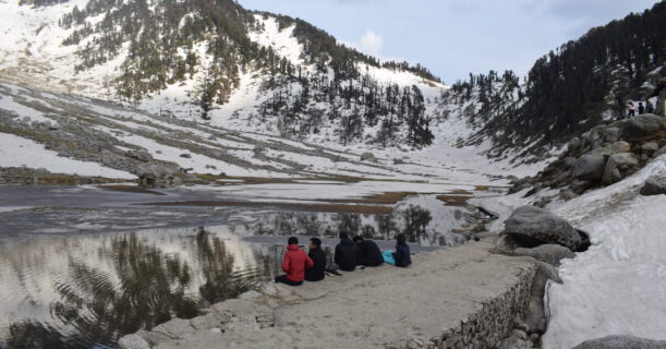 5 boys sitting beside a snow-covered mountain lake with scenic views of the surrounding snowy landscape