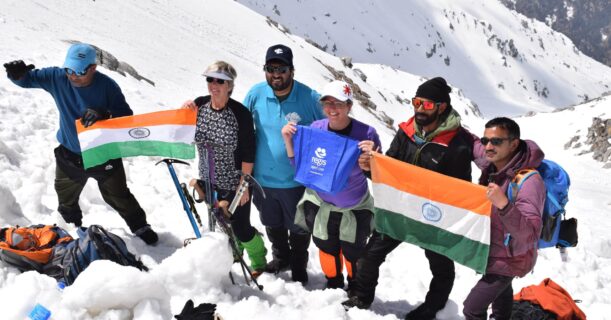 A bunch of trekkers smiling and posing for a picture on a snowy mountain peak.