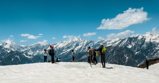 A gathering of individuals standing triumphantly on a snow-covered mountain peak, surrounded by a breathtaking winter landscape.