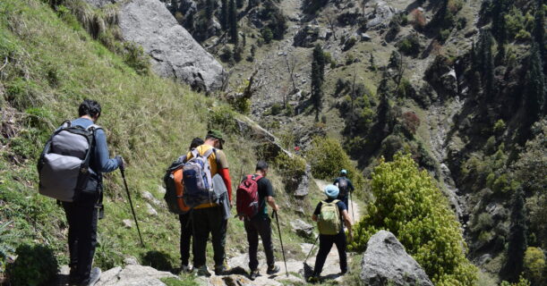 A group of people with backpacks walking down a rocky trail surrounded by greenery