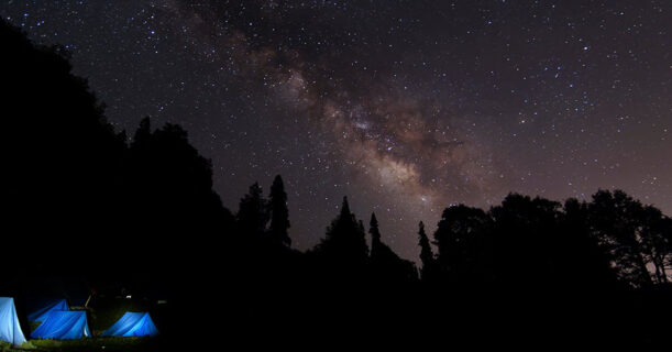 A serene camping scene featuring a tent set up under a starry night sky, surrounded by trees and a peaceful atmosphere.