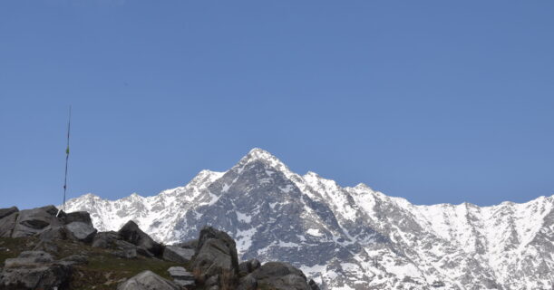 A snow-covered mountain peak featuring a prominent radio tower against a clear blue sky.