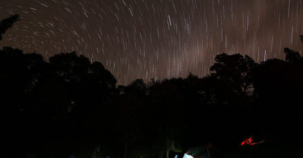 Night sky with star trails above tents, capturing the beauty of camping under the stars