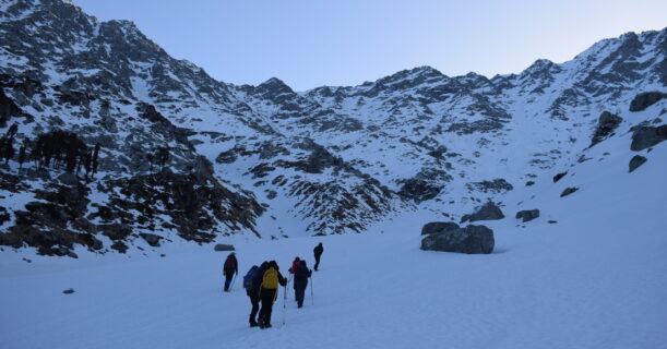 Team trekking up a snow-covered mountain, navigating rocky terrain amidst a winter landscape.