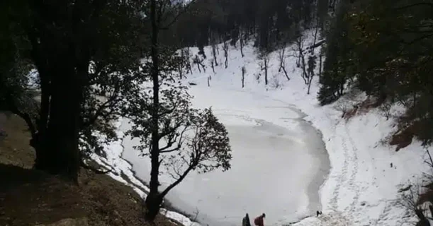 A man traverses a snowy trail near a still-frozen lake, immersed in the peacefulness of a winter scene.