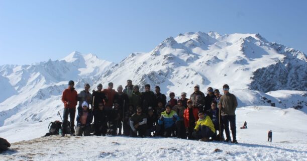 A collection of persons standing on a snowy mountain peak.