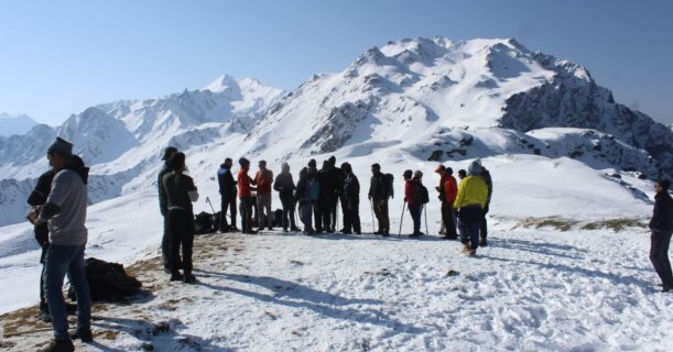 A gathering of people celebrates at the summit of a snow-covered mountain, enjoying the stunning views of the winter scenery.