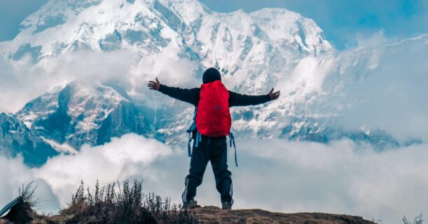 A man standing with arms outstretched on a mountain peak.