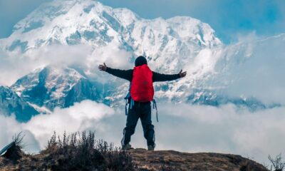 A man stands atop a mountain, arms outstretched, embracing the vast landscape and open sky around him.