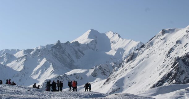 People standing on top of a snow-covered mountain with snow-capped peaks in the background.