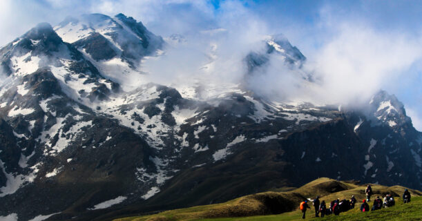 Some Humans walk on the grass near the mountain, enjoying nature.