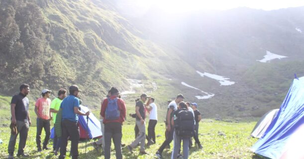 Trekkers standing near tents in a mountainous landscape, enjoy the serene outdoor environment.