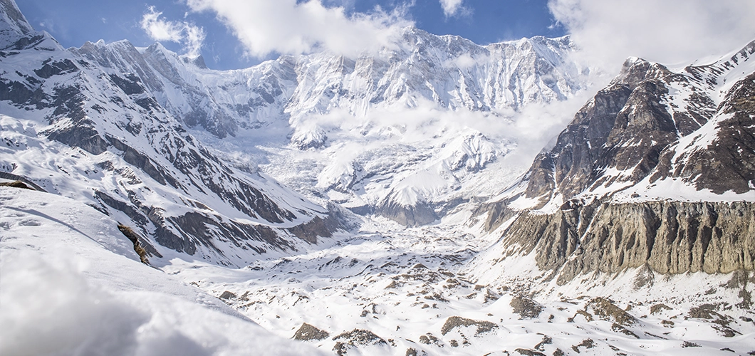 Trekker ascending a snowy mountain pass with majestic peaks in the background.