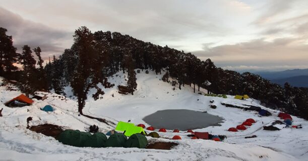 Snow-covered Brahmatal Lake campsite with colorful trekking tents in Uttarakhand Himalayas