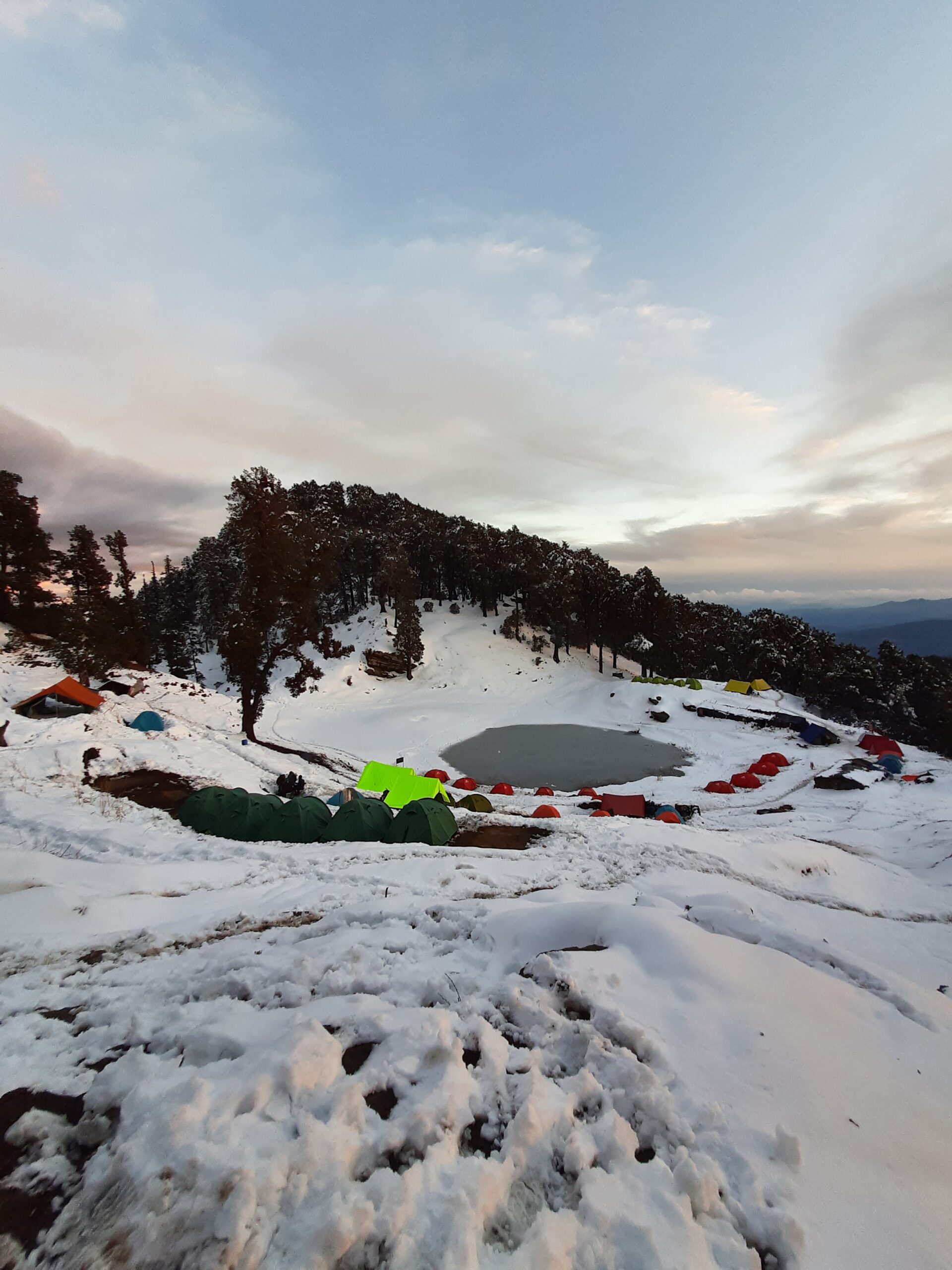 Snow-covered Brahmatal Lake campsite with colorful trekking tents in Uttarakhand Himalayas