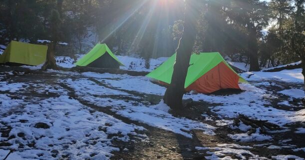 Sunrise over snow-covered Brahmatal campsite with colorful trekking tents in Uttarakhand