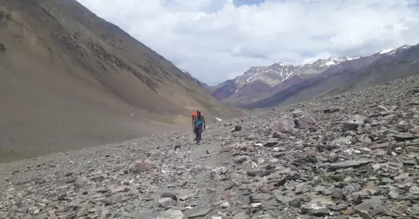Trekkers walking through a barren, rocky trail in Pin Valley after crossing Pin Parvati Pass.