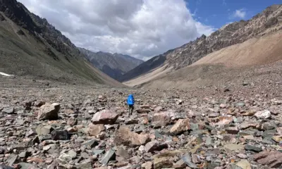 A trekker with a blue backpack walks across a vast, rocky valley in Spiti after descending Pin Bhabha Pass.