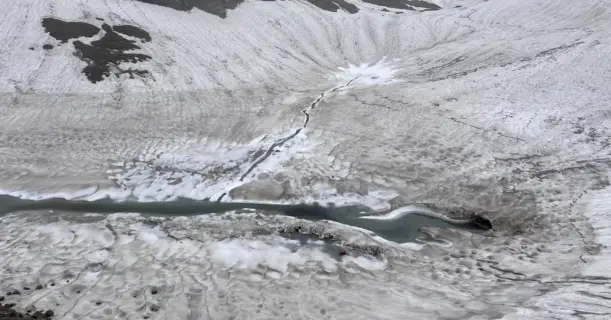 A high-altitude glacier field with a flowing meltwater stream and crevasses on the Pin Bhabha Pass trail.