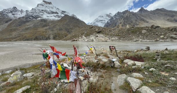 Mantalai Lake on the Pin Parvati Pass Trek, with prayer flags and snow-capped Himalayan peaks in Parvati Valley, Himachal Pradesh