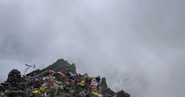 Summit of Pin Bhaba Pass with prayer flags fluttering amid clouds at 4,915 meters