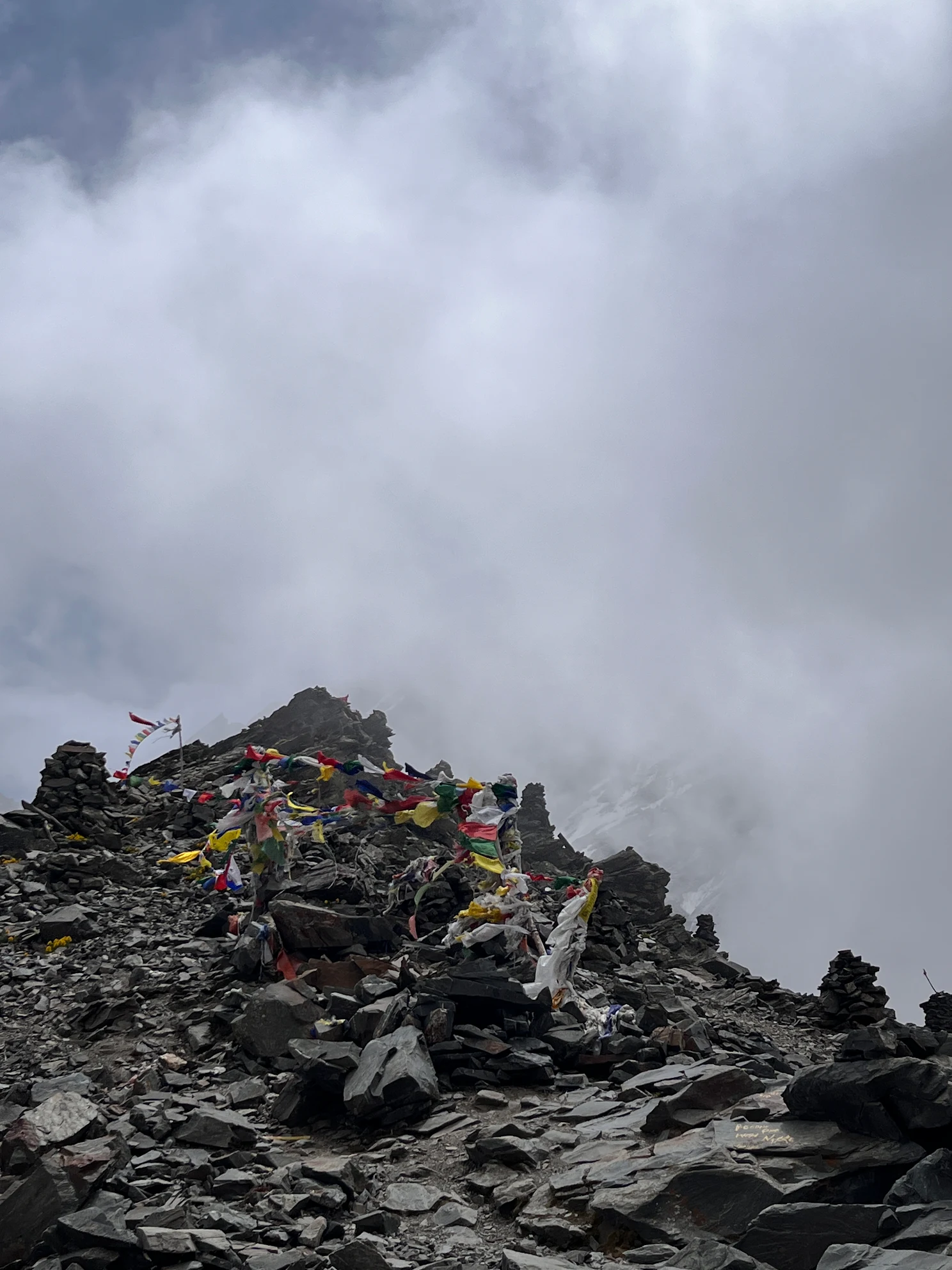 Summit of Pin Bhaba Pass with prayer flags fluttering amid clouds at 4,915 meters