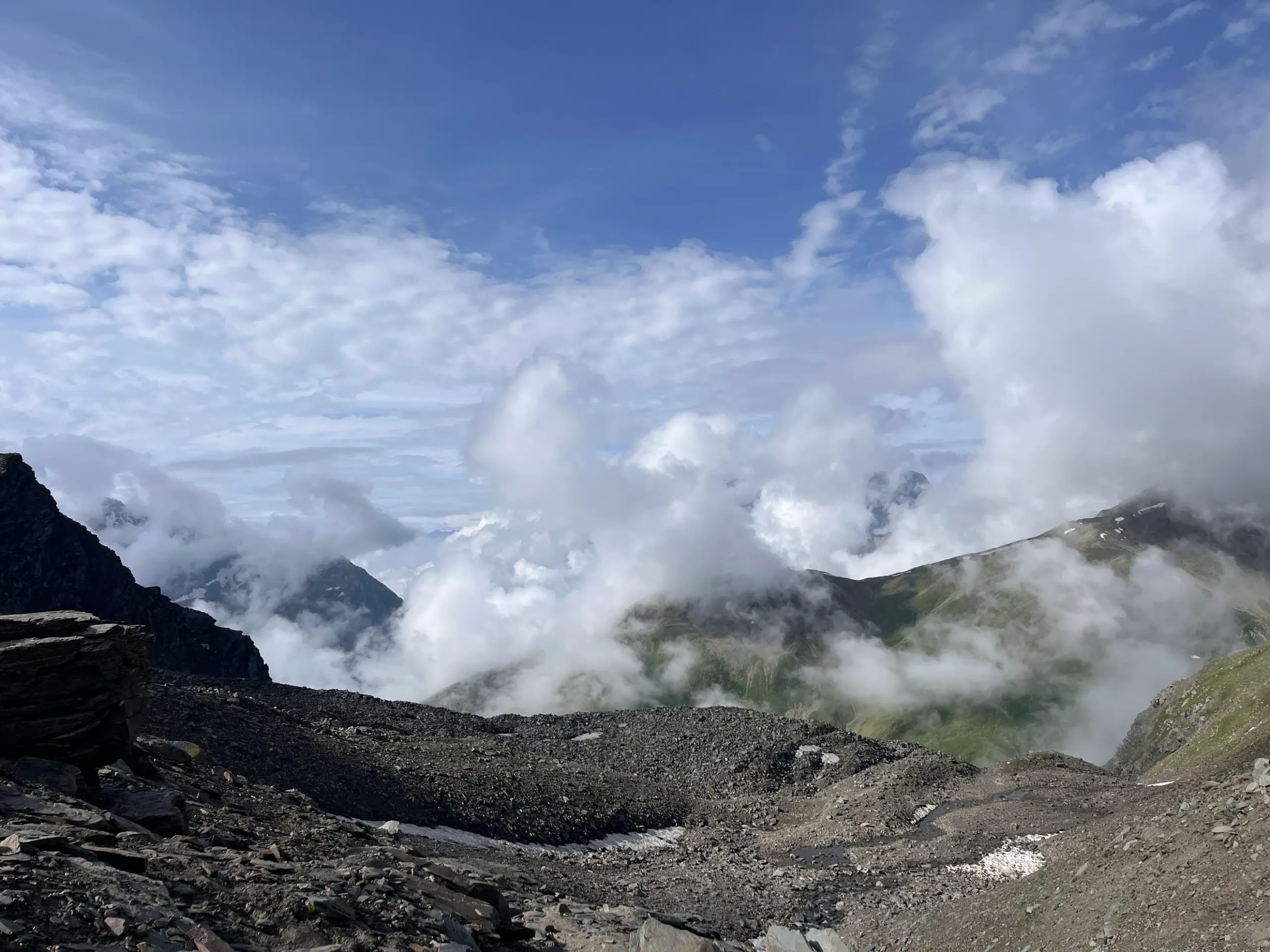View from near Pin Bhabha Pass summit showing dramatic cloudscape over deep valleys and rugged terrain.