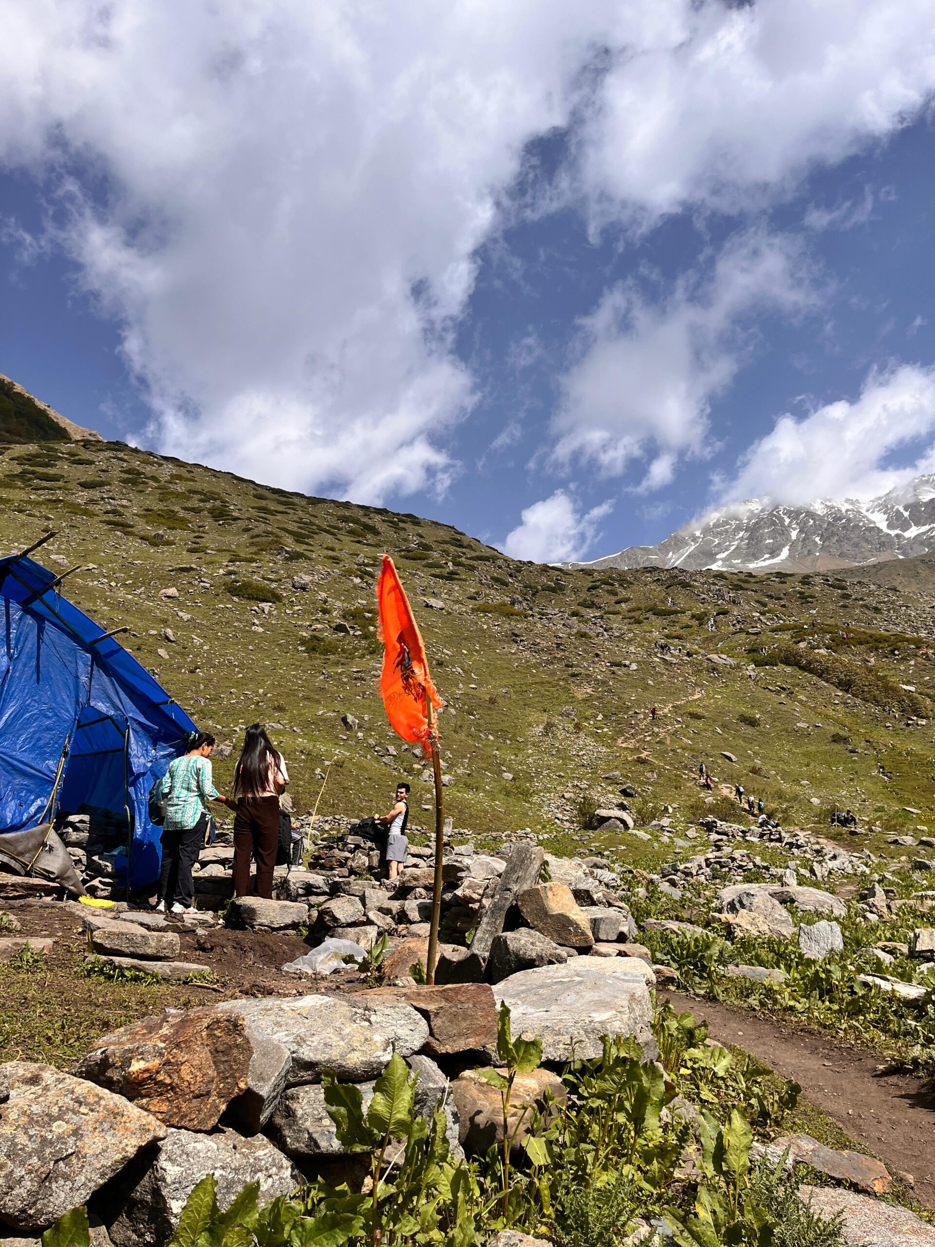 Orange religious flag fluttering at a rest stop on the Yulla Kanda trek trail in Himachal Pradesh with mountain backdrop