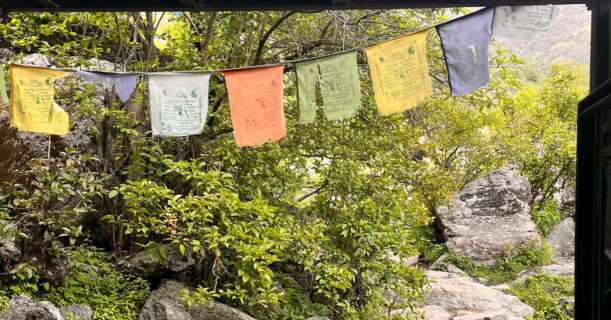 Entrance signboard reading “Welcome to Yulla Kanda” with colorful prayer flags and rocky trekking trail in Himachal Pradesh