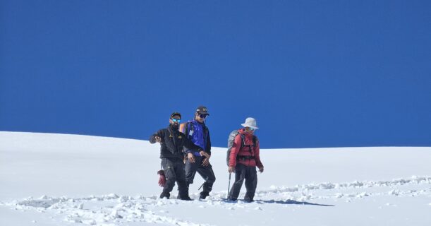 Trekkers ascending the snow ridge during Pangarchulla Peak Trek in Uttarakhand under a clear blue sky.