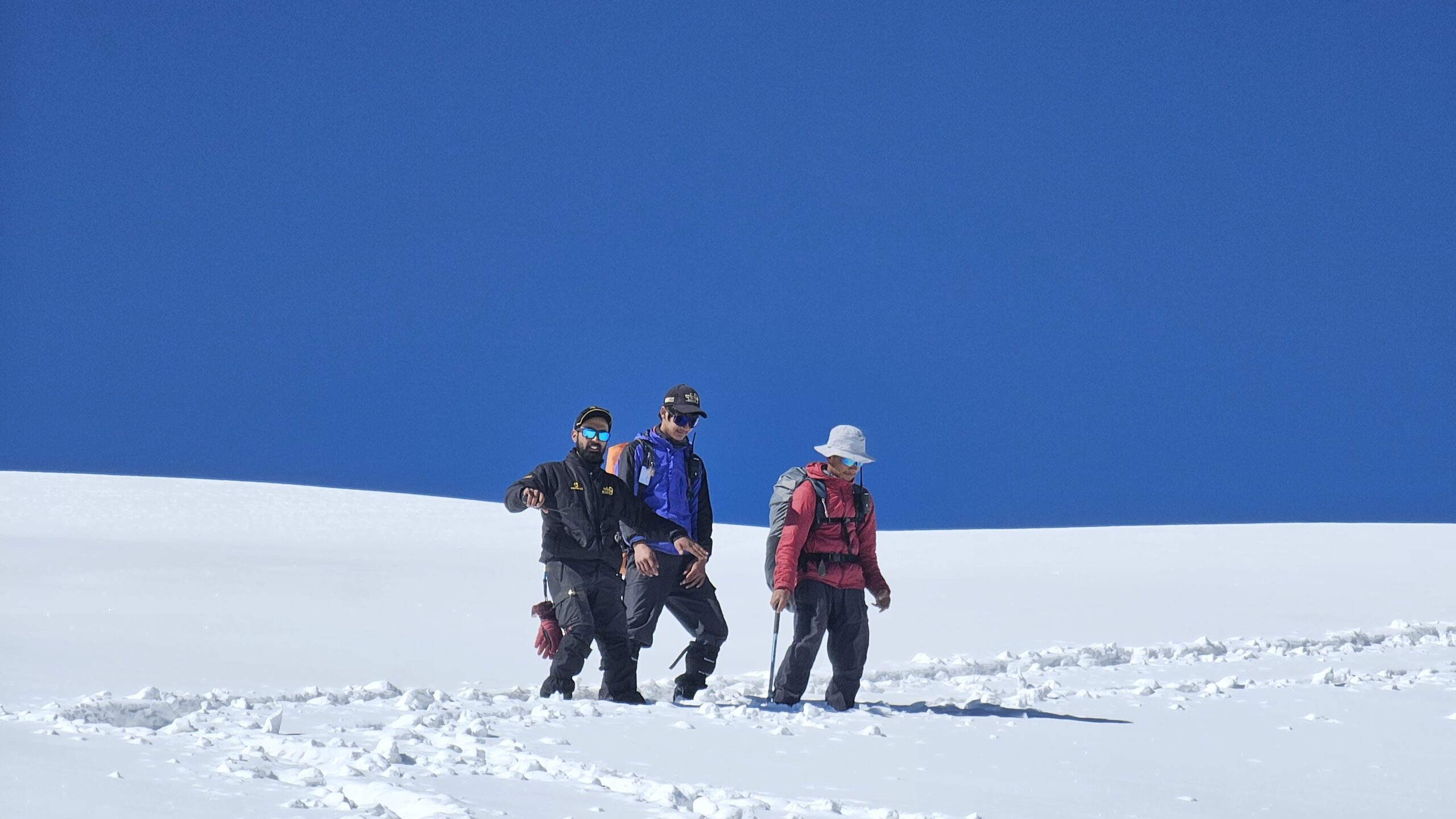 Trekkers ascending the snow ridge during Pangarchulla Peak Trek in Uttarakhand under a clear blue sky.